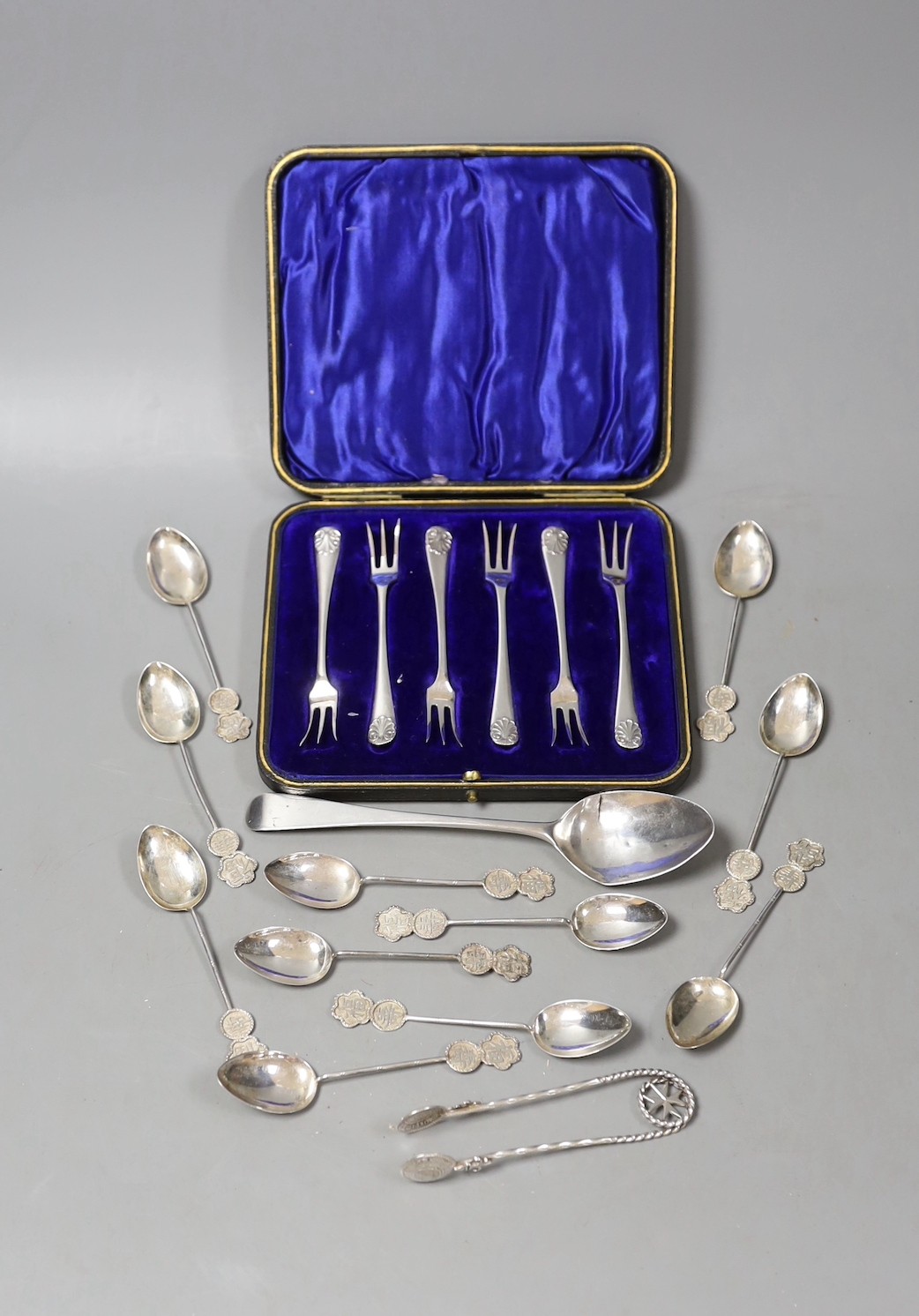A cased set of six George V silver cake forks, a set of eleven Chinese white metal coffee spoons, a Georgian silver dessert spoon and a pair of white metal sugar tongs.